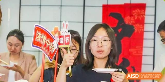 A female student from The Affiliated High School of Peking University's Dalton Academy holding a small decorative sign with a rabbit icon and other decorations, possibly during a cultural festival.