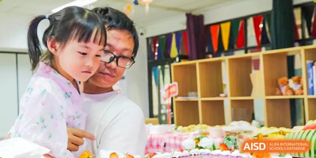 A close-up side profile of a young boy from The Affiliated High School of Peking University's Dalton Academy looking at a table set up with food and activities.