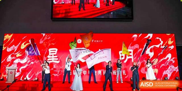 Students from The Affiliated High School of Peking University's Dalton Academy performing a modern dance or routine on a stage with a bright red background.