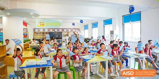 A bright and lively CHONGQING WEIMING SCHOOL classroom with many students participating in a lesson or activity, supervised by a teacher.