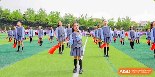 A CHONGQING WEIMING SCHOOL student in uniform holding a flag and singing or speaking on a microphone on the field.