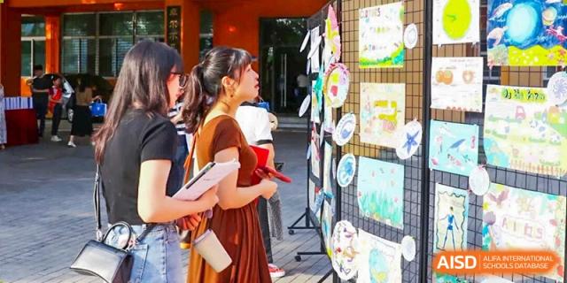 A teacher or parent at CHONGQING WEIMING SCHOOL looking at student artwork displayed outside.