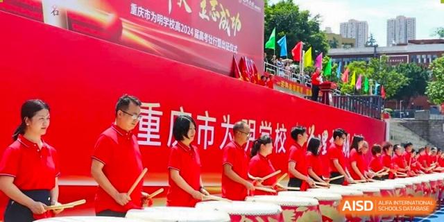 CHONGQING WEIMING SCHOOL students playing drums and standing near a large red banner at an outdoor event.