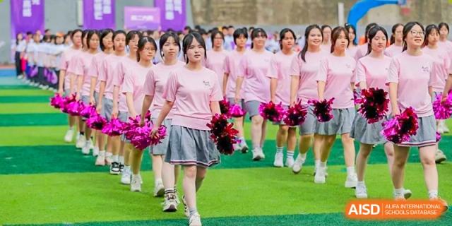 A line of CHONGQING WEIMING SCHOOL female students in pink shirts and skirts marching while holding pom-poms.