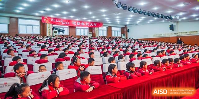 A large group of CHONGQING WEIMING SCHOOL students in red uniforms attending a formal assembly or lecture in a large hall.