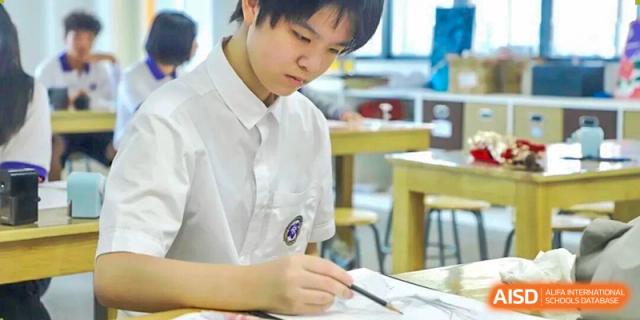 A close-up of a student from Cogdel Cranleigh School Changsha in a white uniform, writing or drawing with a pencil during a class activity.