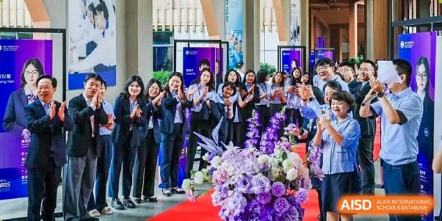 A group of female Cogdel Cranleigh School Changsha students cheering and applauding at a formal school ceremony, with a floral arrangement in the foreground.