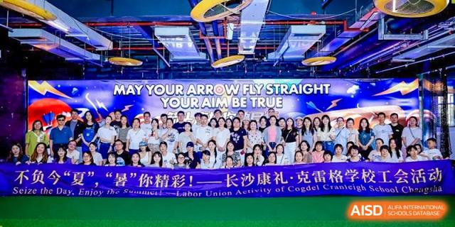 A large group of Cogdel Cranleigh School Changsha students and staff posing for a photo under a banner that reads "YOUR ARROW FLY STRAIGHT, YOUR AIM BE TRUE" during a school event.