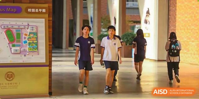 Two male students from Cogdel Cranleigh School Changsha in their school uniform polo shirts and shorts walking along an outdoor corridor or walkway.
