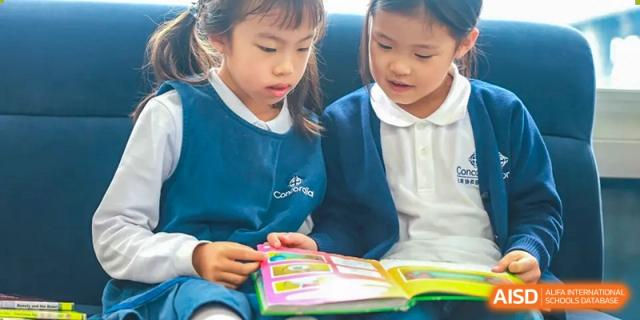 Two young Concordia International School Shanghai students looking closely at a colorful textbook or project book.
