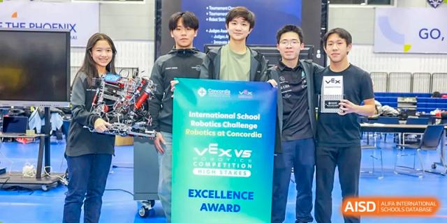 Three high school students from Concordia International School Shanghai posing with their VEX Robotics Competition "Excellence Award" banner after the competition.