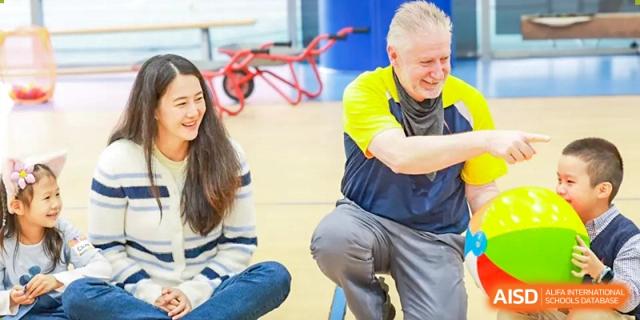 An adult mentor or teacher engaging with students on the floor of the gymnasium at Concordia International School Shanghai.