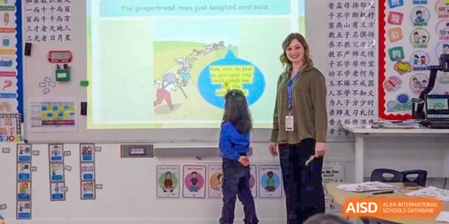A DAYSTAR ACADEMY teacher and a young student interacting in a classroom near a screen or smartboard.