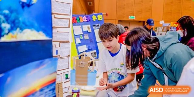 A young male student is engaged in a hands-on activity near a display board during a school event at DAYSTAR ACADEMY.