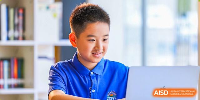 A male DAYSTAR ACADEMY student in a blue polo shirt using a laptop in a classroom setting.
