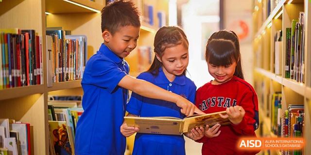 Two young students, a boy and a girl, in school uniform are reading and pointing at a book together in a library or classroom at DAYSTAR ACADEMY.