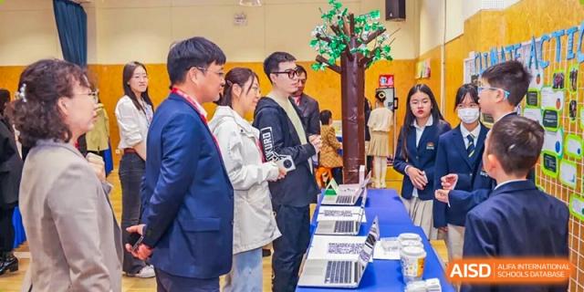 A group of adults, including parents and staff, are viewing laptop computers displayed on a table at a school event at DAYSTAR ACADEMY.