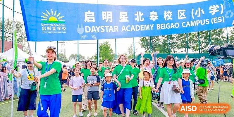 Group of students, teachers, and staff wearing green shirts at a DAYSTAR ACADEMY event with a banner in the background.