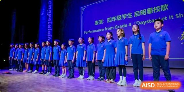 A group of DAYSTAR ACADEMY students from Grade 4 standing on stage after a performance with a blue backdrop.