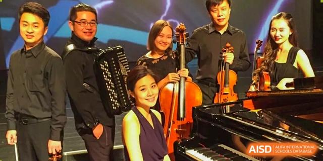 DAYSTAR ACADEMY students and an adult performing music with a cello, piano, and accordion on a stage.