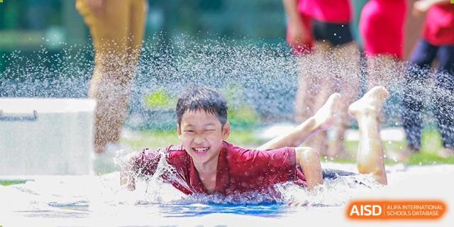 A smiling DAYSTAR ACADEMY student splashing in a pool during a swimming activity.