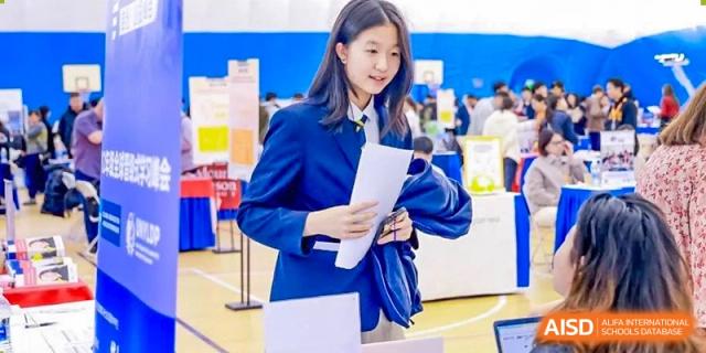 A DAYSTAR ACADEMY female student in a blue school uniform blazer holding papers in a bright indoor setting.