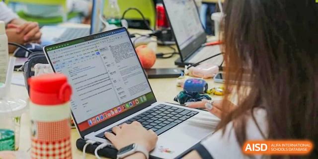 A student working on a laptop open to documents or code, with a bright orange object nearby, Fuyuan British American School.
