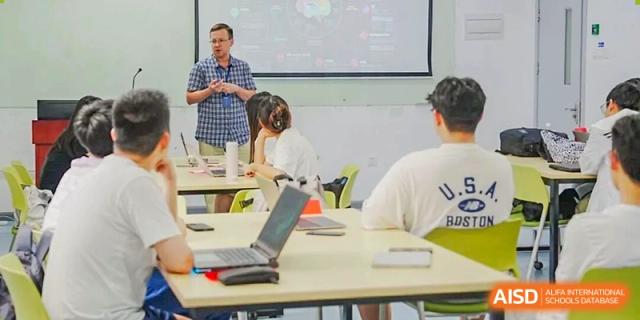Two students sitting at a table with a laptop, engaged in a discussion or collaborative project in a brightly lit classroom, Fuyuan British American School.