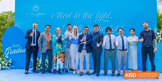 Group photo of diverse staff or faculty members standing together with a blue background featuring the text "Meet in the light," Fuyuan British American School.