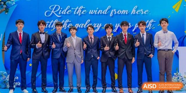A group of male students in dark blue suits giving thumbs-up signs at a formal event with a blue and yellow background, Fuyuan British American School.