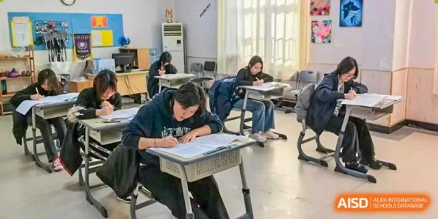A student is focused on writing or taking a test at a desk in a classroom at Guokai International School of Qingdao.