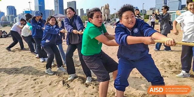 Students and adults participating in a tug-of-war game on a beach at Guokai International School of Qingdao.