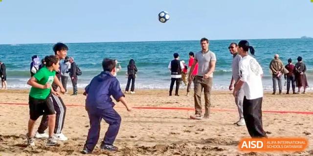 A group of people playing soccer or volleyball on the beach with the ball in the air at Guokai International School of Qingdao.
