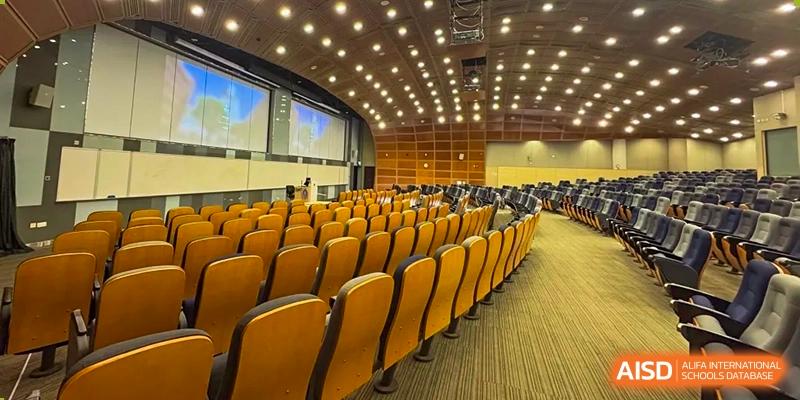 An interior view of a large school auditorium with rows of empty yellow seats facing a stage or screen at Guokai International School of Qingdao.