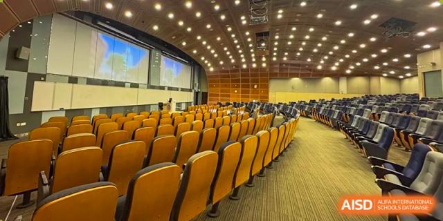 An interior view of a large school auditorium with rows of empty yellow seats facing a stage or screen at Guokai International School of Qingdao.