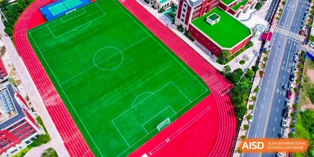 Aerial view of the green soccer field and red running track at Harrow Lide High School Nanning sports complex. Focuses on athletics.