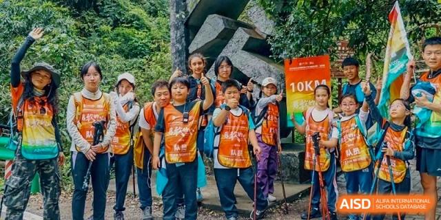Group of happy Harrow Lide High School Nanning students and staff in vests posing during an outdoor nature hiking trip.
