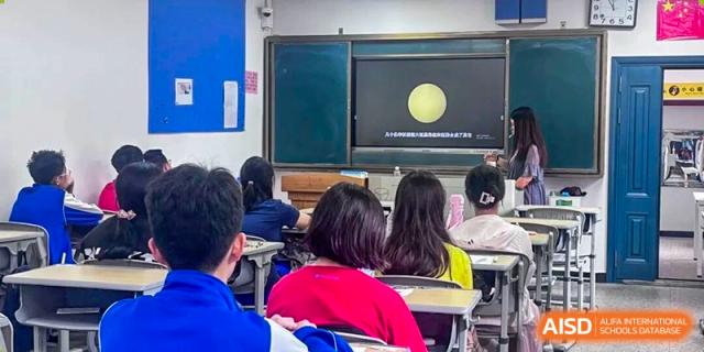 Students from The High School Attached to Hunan Normal University looking towards the front of the classroom where a projection of the solar system or a planet is displayed.