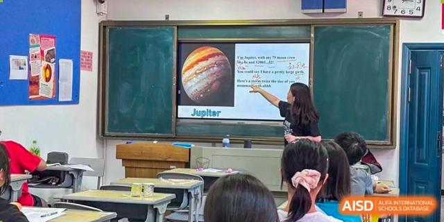 A teacher from The High School Attached to Hunan Normal University pointing to a slide about Jupiter on a screen during a science lesson in the classroom.