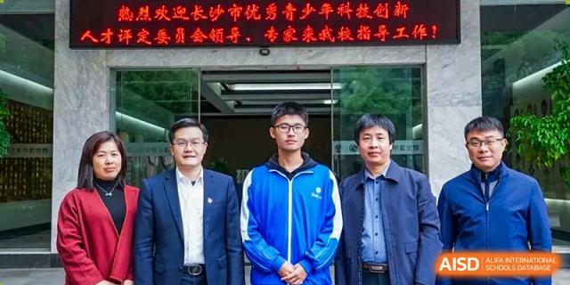 A student from The High School Attached to Hunan Normal University in a blue sports uniform posing for a photo with two adult male staff or faculty members.
