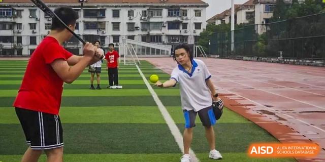 A male student from The High School Attached to Hunan Normal University practicing a baseball or softball pitch on a green sports field during an outdoor activity.