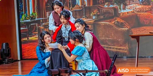 A group of female students from The High School Attached to Hunan Normal University wearing historical or traditional costumes, looking at a document together as part of a performance or cultural activity.