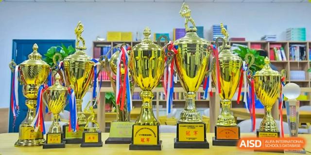 A large display of multiple gold trophies and awards with colorful ribbons, representing student achievements at The High School Attached to Hunan Normal University.
