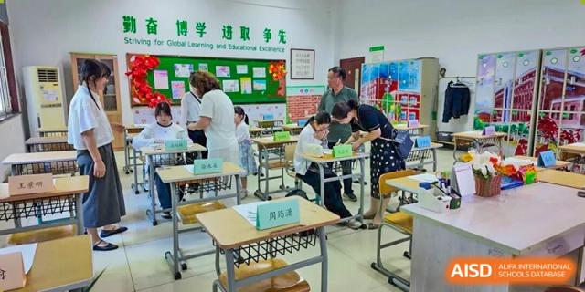 A teacher bending over to help students with a task at their desks in a classroom at Maple Leaf International School-Zhenjiang.