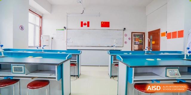 An empty classroom or lab with a whiteboard displaying Canadian and Chinese flags above a row of blue desks at Maple Leaf International School-Zhenjiang.