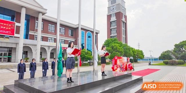 A female student in uniform holding an award or certificate on a set of outdoor stairs at Maple Leaf International School-Zhenjiang.