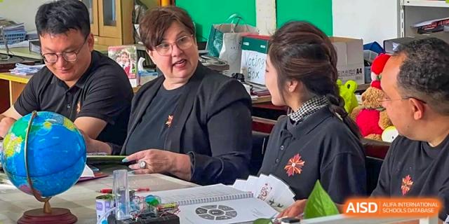 A foreign female teacher in a black top conversing with another adult in an office or meeting setting at Maple Leaf International School-Zhenjiang.
