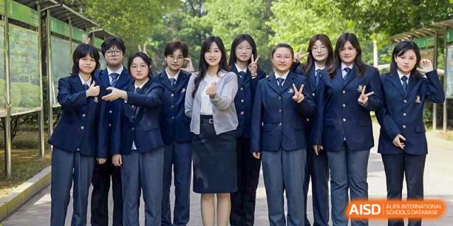 A group of female students and an adult teacher posing for a photo outdoors near trees at Maple Leaf International School-Zhenjiang.