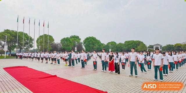 A large group of students in uniform performing a synchronized dance or activity outdoors on a red and white pavement at Maple Leaf International School-Zhenjiang.