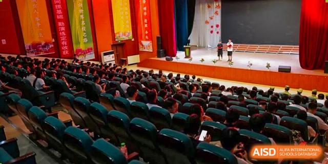 The interior of a large, full auditorium with red seats and a stage with red curtains at Maple Leaf International School-Zhenjiang.